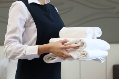 Oda servisi temizliği ve otel odası konsepti. Kadın oda hizmetçisi otel odasında yatak yapmak için temiz beyaz banyo havluları tutuyor..