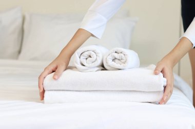 Oda servisi temizliği ve otel odası konsepti, kadın elleri yatak örtüsüne temiz beyaz banyo havluları koyuyor.. 