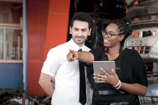 Happy Harmony people at workplace, smiling white man and African American worker working together, two people checking product stock at auto spare parts store shop warehouse with many second hand engine parts as blurred background