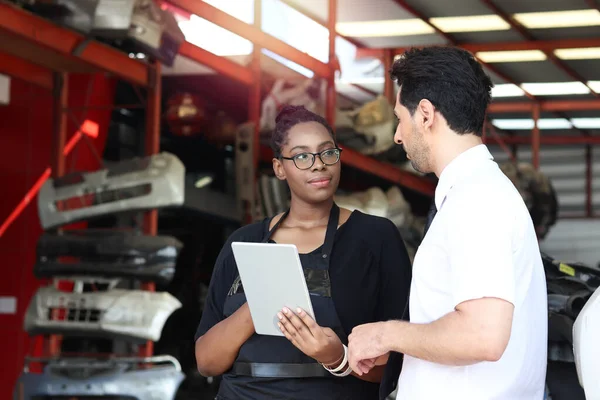 Happy Harmony people at workplace, smiling white man and African American worker working together, two people checking product stock at auto spare parts store shop warehouse with many second hand engine parts as blurred background