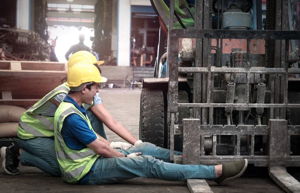 Accident at workplace, industrial engineer worker wearing helmet hit by forklift car at manufacturing plant factory construction site building, man leg stuck in forklift, colleague try to help him