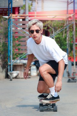 Güneş gözlüğü takan ve güneşli bir günde dışarıda sörf yapan Asyalı genç adam, kaykayla dışarıda eğlenmenin tadını çıkarıyor..