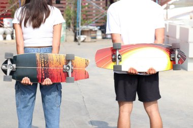 İnsanlar arkalarında sörf tahtası tutuyorlar, gençler güneşli bir günde açık havada kaykay sporu yaparak eğleniyorlar..