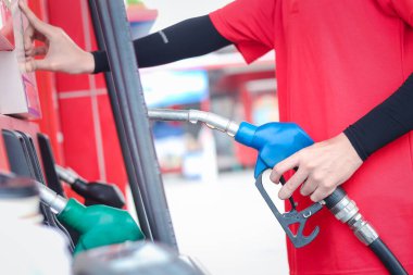 Benzin istasyonunda benzin pompası tutan kırmızı üniformalı bir görevli var..