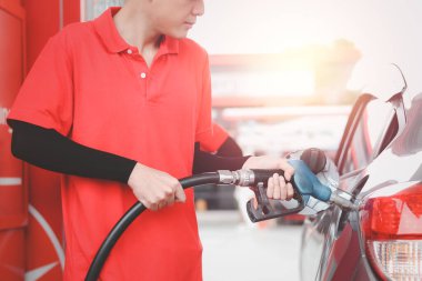 Benzin pompası başlığı tutan kırmızı üniformalı bir benzinci benzinlikteki benzin deposunu benzinle doldurmaya karşı..