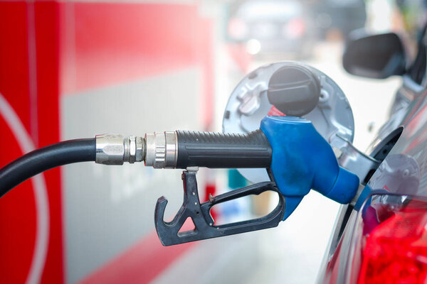 Close up of blue fuel petrol pump nozzle against for filling up the red car with petrol at gas station.