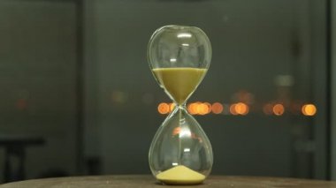 Kum saati şehir gece lambasıyla zamanı ölçüyor. Arka plan bulanık. Kum saatine düşen sarı kum saati..