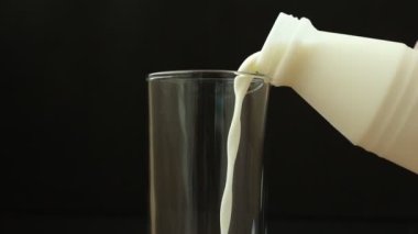 Şişeden siyah arka planda bardağa süt dökülüyor.. 