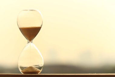 Kum saati, akşam vakti turuncu gökyüzü ile şehri ölçüyor. Arka planda bulanıklık var. Sarı kum, kum saatine düşüyor..