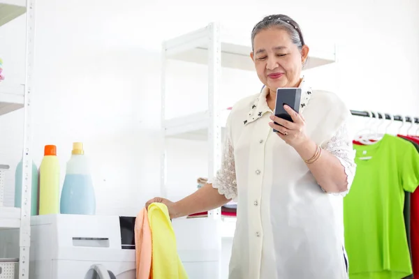 Счастливая Пожилая Азиатская Домохозяйка Пользующаяся Мобильным Телефоном Время Стирки Комнате — стоковое фото