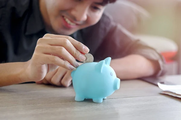 机の上の青い貯金箱にコインを集める幸せな笑顔の若いアジア人男性 将来の概念のための財政貯蓄や投資 — ストック写真