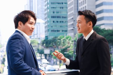 Takım elbiseli iki başarılı iş adamı şehir merkezindeki gökdelen binası hakkında konuşuyor ve tartışıyorlar. İş adamları ofis dışında buluşuyorlar..