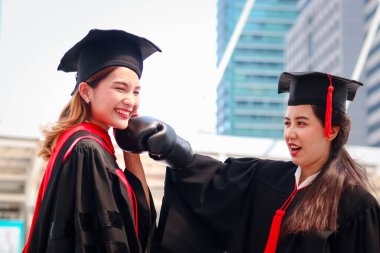 İki mutlu mezun kadın öğrenci, akademik şapka şapkasını kırmızı boks eldiveni ya da eldiven yumruğuyla ısıtıyorlar. Hayat, mezuniyet gününde başarılı bir eğitimi kutladıktan sonra bölge kavgası demektir..