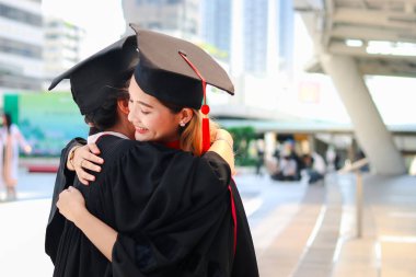 Kare akademik şapkalı iki mutlu mezun kadın öğrenci birbirine sarılıyor, başarılı eğitimi kutluyor ve üniversite ya da üniversite eğitimini bitirdikten sonraki mezuniyet gününde arkadaşlarıyla kutlama yapıyorlar..