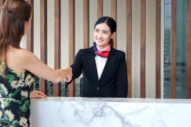 Mutlu, gülümseyen, takım elbiseli, Asyalı genç bayan resepsiyonist otel resepsiyonunda müşteriyle el sıkışıyor, otel servisinde tatil konsepsiyonunu kontrol ediyor.. 