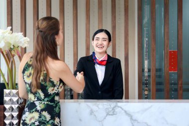 Mutlu, gülümseyen, takım elbiseli, Asyalı genç bayan resepsiyonist otel resepsiyonunda müşteriyle el sıkışıyor, otel servisinde tatil konsepsiyonunu kontrol ediyor.. 