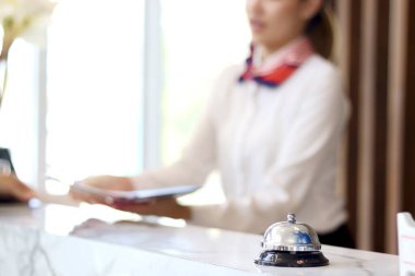 Otel resepsiyonundaki gümüş zil zilinin yakın plan görüntüsü. Otel resepsiyonundaki müşteri bulanık arka plan olarak görünüyor.. 
