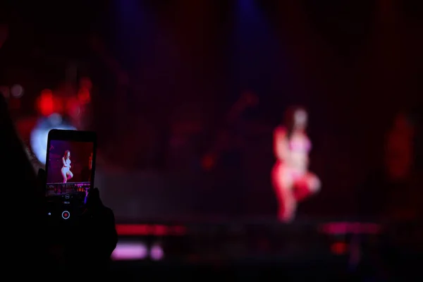 観客はステージ上で踊るセクシーな女性の写真やビデオを撮影します 暗い背景にカラフルな輝き明るいスポットライトとステージコンサートで示す女の子 — ストック写真