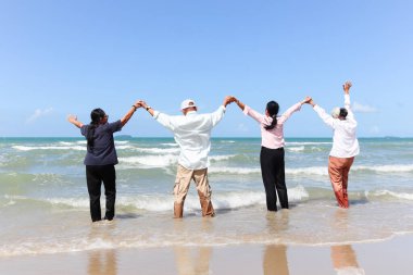 Dört neşeli, yaşlı, yaşlı arkadaş grubu kumsalda koşarken el ele tutuşup, el ele tutuşarak, tatilde dinlenerek ve dinlenerek vakit geçiriyorlar.. 