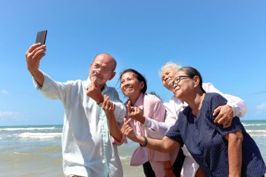 Dört yaşlı, kıdemli arkadaştan oluşan bir grup birlikte dışarı çıkıyor, cep telefonuyla selfie çekiyor, kumsalda eğleniyor ve tatilde dinleniyor ve dinleniyor..