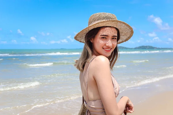 Portrait of beautiful Asian woman with big hat and sunglasses enjoy spending time on tropical sand beach blue sea, happy smiling female resting and relaxing on summer holiday vacation.