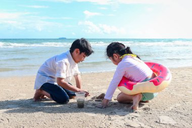 İki tatlı çocuk kumlu yaz kumsalında birlikte eğleniyor mavi denizle, mutlu çocukluk arkadaşı tropik sahilde kumla oynuyor, erkek ve kız kardeş aile tatilinde vakit geçiriyor..