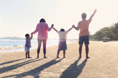 Mutlu dört kişilik aile yaz tatilinde birlikte vakit geçirir ve eğlenir neşeli ebeveynler çocuklar tropikal deniz kumsalında el ele tutuşur ve dinlenir ve rahatlatıcı bir hafta sonu geçirirler..