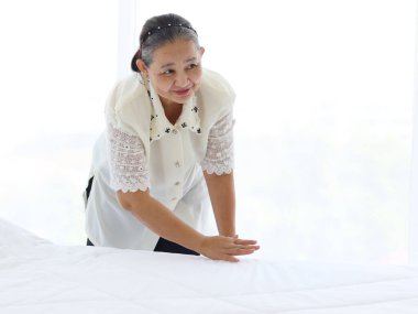 Mutlu gülümseyen Asyalı yaşlı ev hanımı yatak odasını temizliyor, büyükannem ev işi yapıyor ve temizlik yapıyor, yaşlı kadın oda hizmetçisi beyaz battaniye ve çarşafı değiştiriyor.