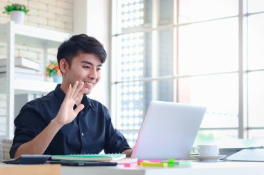 Siyah tişörtlü Asyalı genç iş adamı video konferansında iş arkadaşlarıyla bilgisayar kullanarak görüntülü görüşme ve iletişim kuruyor..