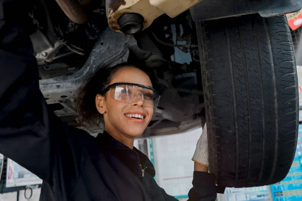 女性の自動車整備士の作業ガレージ 車サービス技術者の女性は 自動車サービスセンターで顧客の車を確認し 修理し ボディとサスペンションシステムの下で車を検査し 車両修理サービスショップ — ストック写真