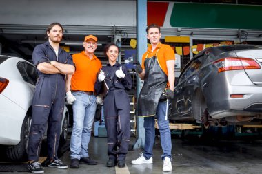 Dört araba servisi teknisyeni ve kadın kameraya baş parmak işareti yapıyor. Araç tamirhanesinde birlikte çalışan insanlar. Otomobil servis merkezindeki müşteri arabasını kontrol edip tamir ediyorlar.