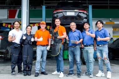 7 kişilik bir grup araba servisi teknisyeni ve kadın işyerinde kuyrukta bekliyor, insanlar araç tamirhanesinde birlikte çalışıyor, otomobil servis merkezindeki müşteri arabasını kontrol edip tamir ediyorlar..