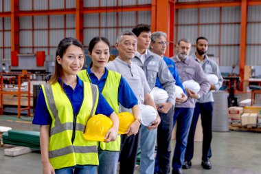 Bir grup mutlu mühendis imalat fabrikasında sıraya dizildi. Mühendislerin miğferi vardır, sanayi bölgesinde güvenle dururlar. Çeşitli profesyonel takımlar kameraya vizyonlarla bakar..