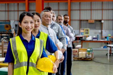 Bir grup mutlu mühendis imalat fabrikasında sıraya dizildi. Şirket mühendisleri şapka başlığı takıyor, sanayi bölgesinde güvenle duruyorlar. Çeşitli takımlar görüntülerle aynı yöne bakıyor..