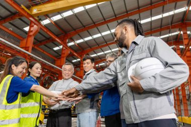 Bir grup mutlu mühendis imalat fabrikasında dururken el ele tutuşuyor. Endüstriyel alanda çeşitli mühendislik ekipleri el ele tutuşuyor. Birlik, dostluk, uyum, takım çalışması konsepti