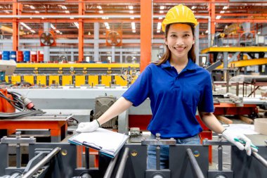 Güvenlik kaskı takan Asyalı kadın bir pano tutuyor, imalat fabrikasında çalışıyor. Kadın mühendis, endüstriyel alandaki metal levhaları inceliyor. Müfettiş ürünün kalitesini kontrol ediyor..