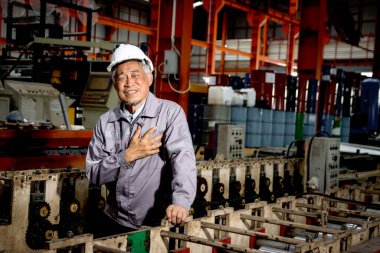 Güvenlik kaskı takan Asyalı kıdemli ustabaşı imalat fabrikasında makineleri incelerken kalp krizi geçiriyor. Yaşlı işçinin sanayi bölgesinde çalışırken göğsünde ağrı var.