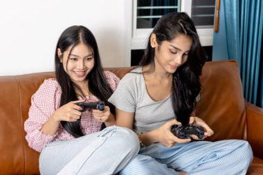 İki genç Asyalı kadın oyun kumandasını oturma odasında oyun oynamak için birlikte tutuyorlar. Genç arkadaşlar çevrimiçi video oyunu oynamaya ve eğlenmeye hazırlar. Dijital teknoloji eğlencesi.