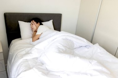 Güzel Asyalı kadın yatak odasında rahat bir yatakta uyuyor. Genç ve güzel bir bayan rahat bir yatakta uyuyor. Uykucu kız mışıl mışıl uyuyor ve sabah uyanmak istemiyor..