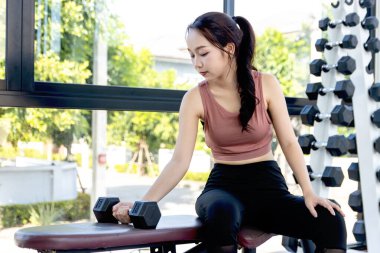 Genç Asyalı kadın spor salonunda dambılını kaldırıyor. Güzel fitness kızı egzersiz yapıyor, vücudu güçlü ve formda tutmak için antrenman yapıyor, sağlıklı yaşam tarzı ve vücut geliştirme.