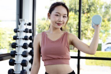 Spor salonunda halterle egzersiz yapan gülümseyen güzel Asyalı kızın portresi. Genç fitness kızı egzersiz yapıyor, vücudu güçlü ve formda tutmak için antrenman yapıyor, sağlıklı ve vücut geliştiriyor..
