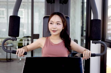 Spor aletleriyle spor yapan Asyalı güzel bir kadın. Genç fitness kızı göğüs pres makinesi kullanıyor. Vücut geliştirme, vücut geliştirme ve dayanıklılığını korumak için antrenman yapıyor..