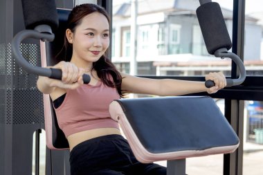 Spor aletleriyle spor yapan Asyalı güzel bir kadın. Genç fitness kızı göğüs pres makinesi kullanıyor. Vücut geliştirme, vücut geliştirme ve dayanıklılığını korumak için antrenman yapıyor..