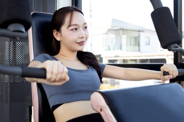Spor aletleriyle spor yapan Asyalı güzel bir kadın. Genç fitness kızı göğüs pres makinesi kullanıyor. Vücut geliştirme, vücut geliştirme ve dayanıklılığını korumak için antrenman yapıyor..