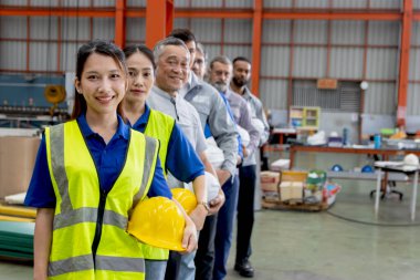 Bir grup mutlu mühendis imalat fabrikasında sıraya dizildi. Mühendislerin miğferi vardır, sanayi bölgesinde güvenle dururlar. Çeşitli profesyonel takımlar kameraya vizyonlarla bakar..