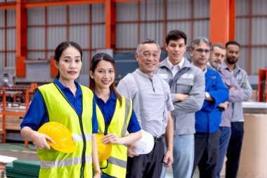 Bir grup mutlu mühendis imalat fabrikasında sıraya dizildi. Mühendislerin miğferi vardır, sanayi bölgesinde güvenle dururlar. Çeşitli profesyonel takımlar kameraya vizyonlarla bakar..
