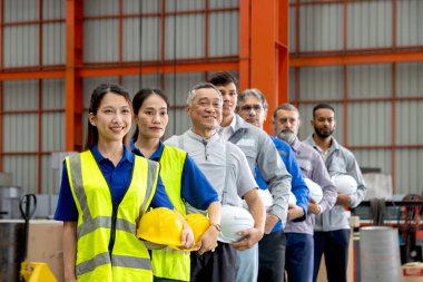 Bir grup mutlu mühendis imalat fabrikasında sıraya dizildi. Şirket mühendisleri şapka başlığı takıyor, sanayi bölgesinde güvenle duruyorlar. Çeşitli takımlar görüntülerle aynı yöne bakıyor..