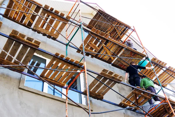 Workers on scaffolding are engaged in plastering the facade. Repair of walls of the house using cement mixtures