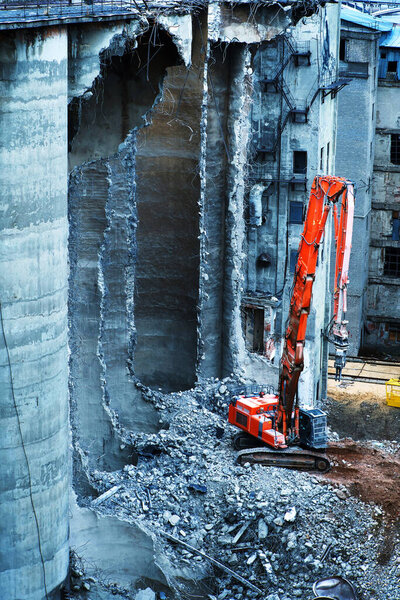 Dismantling a dilapidated building using heavy equipment. Reinforced concrete cutting with hydraulic scissors. Vertical photo