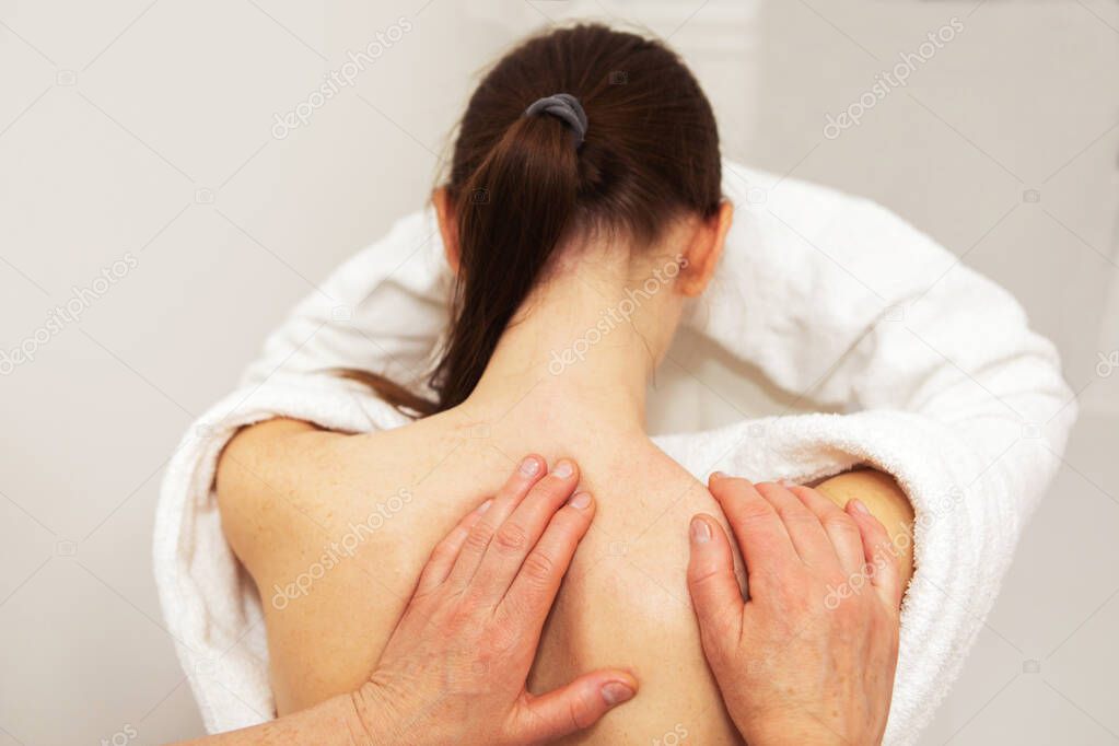 Shoulder massage for a young woman sitting on a chair. The view from the back. No face.